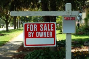 Home for sale by owner real estate sign hanging from a wooden post in the front yard.