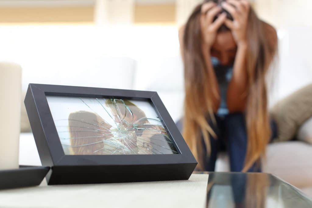 Sad wife sitting on a couch at home with a broken picture